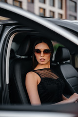 Stylish young girl sitting in a business class car in a black dress. Business fashion and style