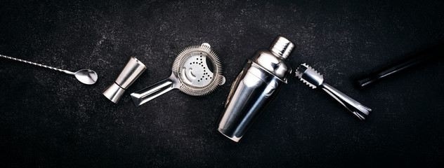 Steel bar tools and accessories for making cocktail. Shaker, jigger, strainer, spoon, tongs, muddler. Alcohol drink and beverages preparation concept. Black background, top view, copy space