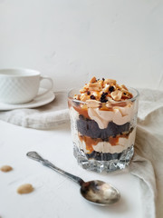 Chocolate dessert with salted caramel and peanuts in a glass on a light background. Individual desserts for a tea party.