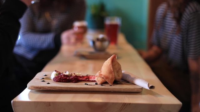 Selective focus of freshly fried and baked single samosa on tray served with red garlic paste, and sauce kept on table with friends drinking wine