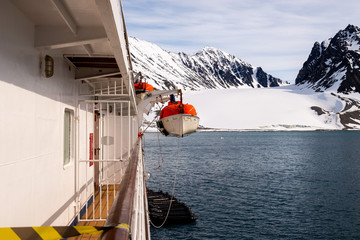 Lowering orange lifeboat to water in Arctic waters, Svalbard. Abandon ship drill. Lifeboat...