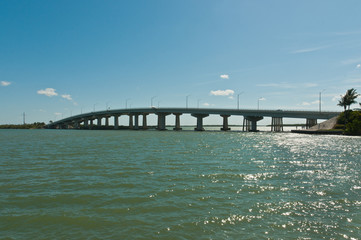 front view, very far distance of a newly constricted, concrete bridge from a tropical mainland and an island on a sunny, spring day