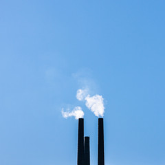 qualmende Industrieschornsteine vor blauem Himmel