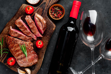 grilled beef steak with spices on a cutting board and a bottle of red wine, glasses on a stone background