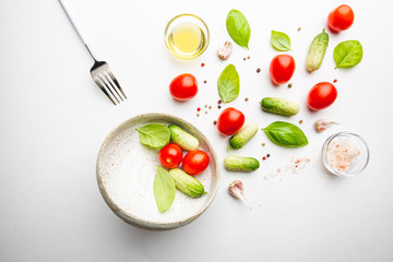 Fresh cut salad ingredients falling into white bowl on white minimal background. Ingredients for making dieting healthy vegetable salad.