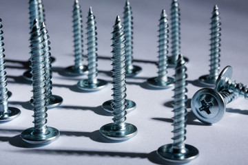 Metal screws stand neatly in a row on a white background.Imitation of a bullet.Shadows from the...