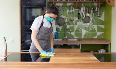 Woman in mask and gloves cleaning kitchen electric ceramic hob