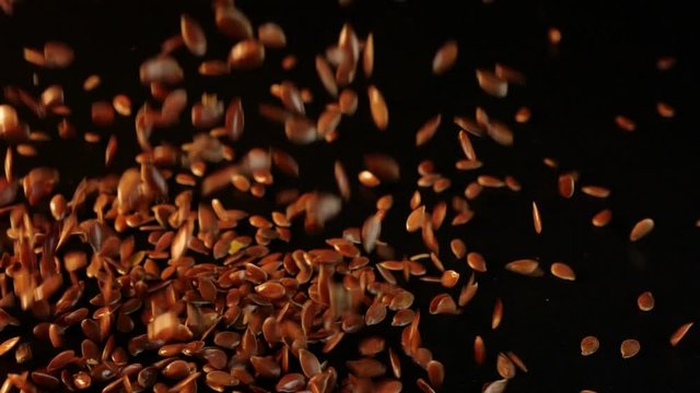 Flaking seeds of flax on a smooth table in a black background. Isolated flax seeds fly down and crumble to the surface. Flax seeds are rich in various minerals and vitamins. Useful product for humans.