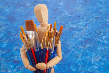 a wooden mannequin holding brushes 
