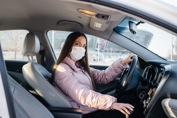Naklejka premium A young girl sits behind the wheel in the car in the mask during the global pandemic and coronavirus. Quarantine