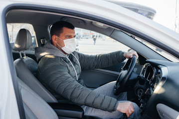 A young man sits behind the wheel wearing a mask for personal safety while driving during a pandemic and coronavirus. Epidemic