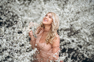 Woman with gorgeous smile, curly blond hair in red dress having fun in blooming garden