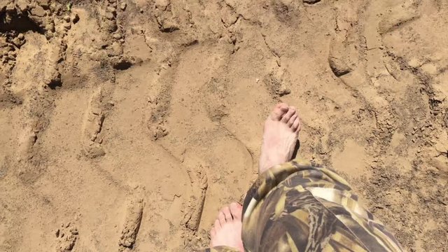 From the first person shot on an iphone 6S, male legs walking on a sandy surface on a hot sunny day