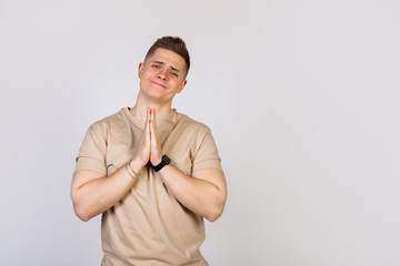 Handsome young man holding his palms pressed together, asking for forgiveness after a quarrel,...