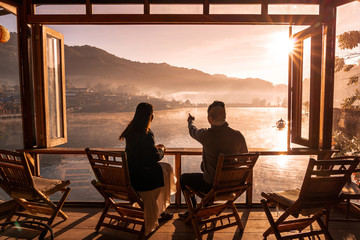 Young asian lover couple sitting on chair look at Sunrise in morning view mist