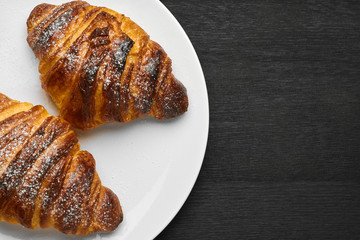 Top view on two fresh french buttery croissant on a white plate on a black background with copy space