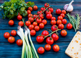 Some red fresh tasty cherries, green spring  onions, green rosemary, leaves of  coriander, sweet cheese, garlic on dark  rustic wooden background