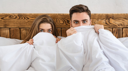 Fear concept. Husband and wife hiding at blanket and watching movie