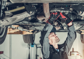 Mechanic Fixing Car Hoisted Up On Hydraulic Lift.