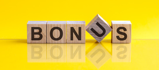 BONUS - word from wooden blocks with letters, concept, yellow background.