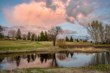 Towering pink sunset cloud over the Swift Current Creek on a golf course in Swift Current, SK, Canada