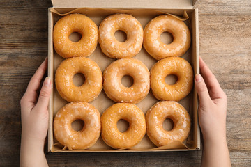 Woman with box of delicious donuts at wooden table, top view