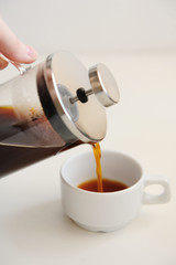 Pouring coffee from french press into white cup. White background