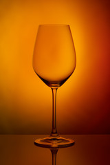 The crystal glass stands on the reflecting surface on a orange red background. studio photo. product. Beautiful shadow from wine glass. macro photo