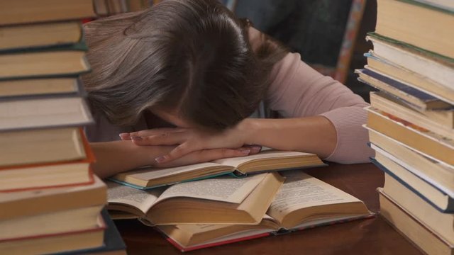 Tired Girl at Table Among Books at Home. Young Woman Student Doing Homework and Falls Asleep. Woman Studying. Home Learning. Distance Education. Smart Clever Woman. Self Teaching. Knowledge University