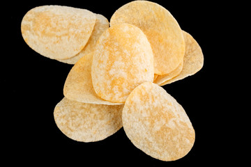 Classic potato chips. Fast food snack isolated on black background. A pile of crispy chips close-up as a background. Unhealthy food.
