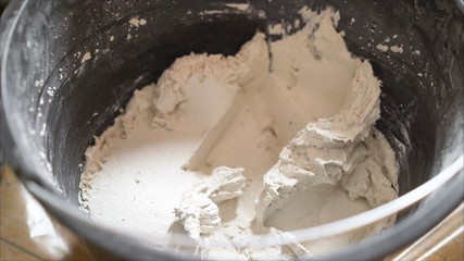 House painter plasterer stirs the putty in a bucket with a handheld mixe. Builder using plaste. Mixed putty in a black bucket.