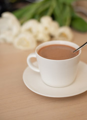 Cup with cacao and saucer on the table, white tulips; morning Breakfast with cacao