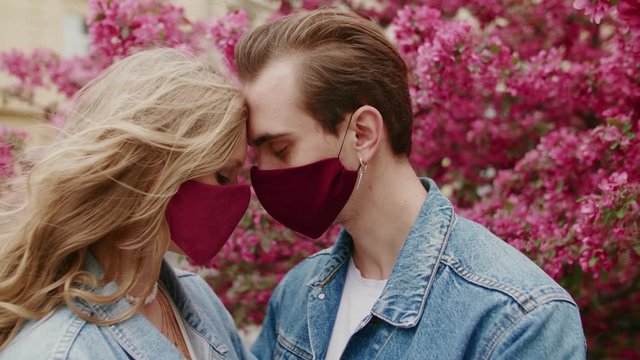 Couple Kissing With Protective Masks. Love During Quarantine Of Coronavirus Pandemic Conception. Man And Woman Posing Near Spring Blossom Pink Trees. Valentines Day.