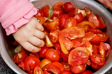 A small child eats tomatoes in the summer. A child taking food. Children's little hand in a summer salad. Playing child. Children's hand in food close-up
