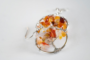Amber semiprecious stones in the shape of a tree in a circle in the shape of an earring on a white background.