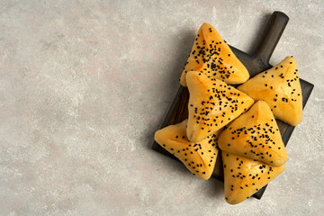 Fatayer pie samosa with white cheese and black sesame seeds on wooden board.