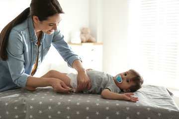 Mother changing baby's diaper on table at home