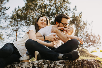 Family of three: man, woman and little girl having fun outdoors. Father kissing daughter on cheek.