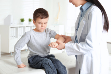 Professional orthopedist examining little patient's arm  in clinic