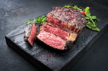 Gegrilltes dry aged Wagyu Entrecote Steak vom Rind mit Salat und Salz als closeup auf einem verkohlten Holz Board