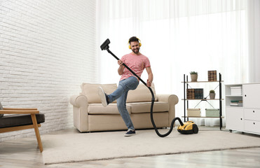 Fototapeta na wymiar Young man having fun while vacuuming at home