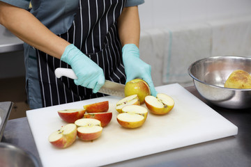 Woman in protective gloves slicing fresh apples on cutting board