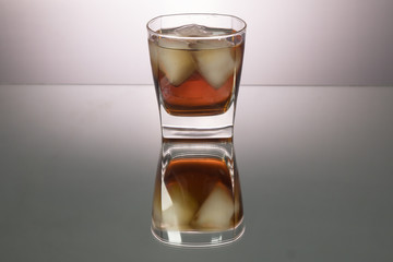 Glass of whiskey with pieces of ice on mirroring table. Horizontal image with copy space.