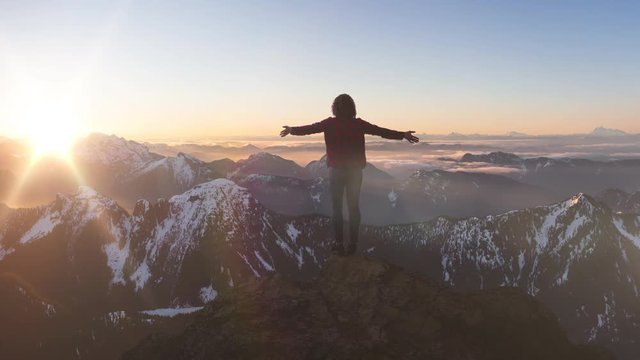 Fantasy Adventure Composite with a Girl on top of a Rock Cliff with Beautiful Canadian Mountain Nature Landscape in Background during Sunset or Sunrise. 2.5D Parallax