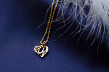 Beautiful gold jewelry chain with heart-shape pendant on dark blue silk background decorated with...