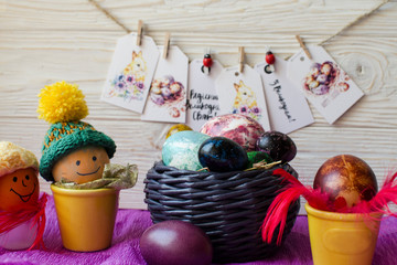 Easter painted eggs in wicker basket decorating with red feathers, knitting hats and little clothespins on wooden background