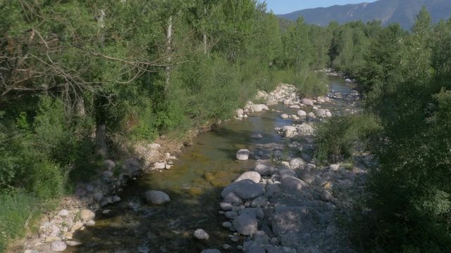 AERIAL DRONE FORWARD SHOT FOLLOWING RUNNING WATER AND RIVER THROUGH FOREST WITH BIG ROUND ROCKS