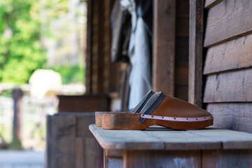 Wooden slippers with a leather upper, placed on an old, wooden table by the wall of the house with...