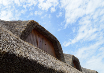 Traditional rural thatched house with brown windows, clear summer sky and some white clouds