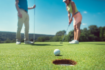 Couple playing golf with the woman on green to hole in